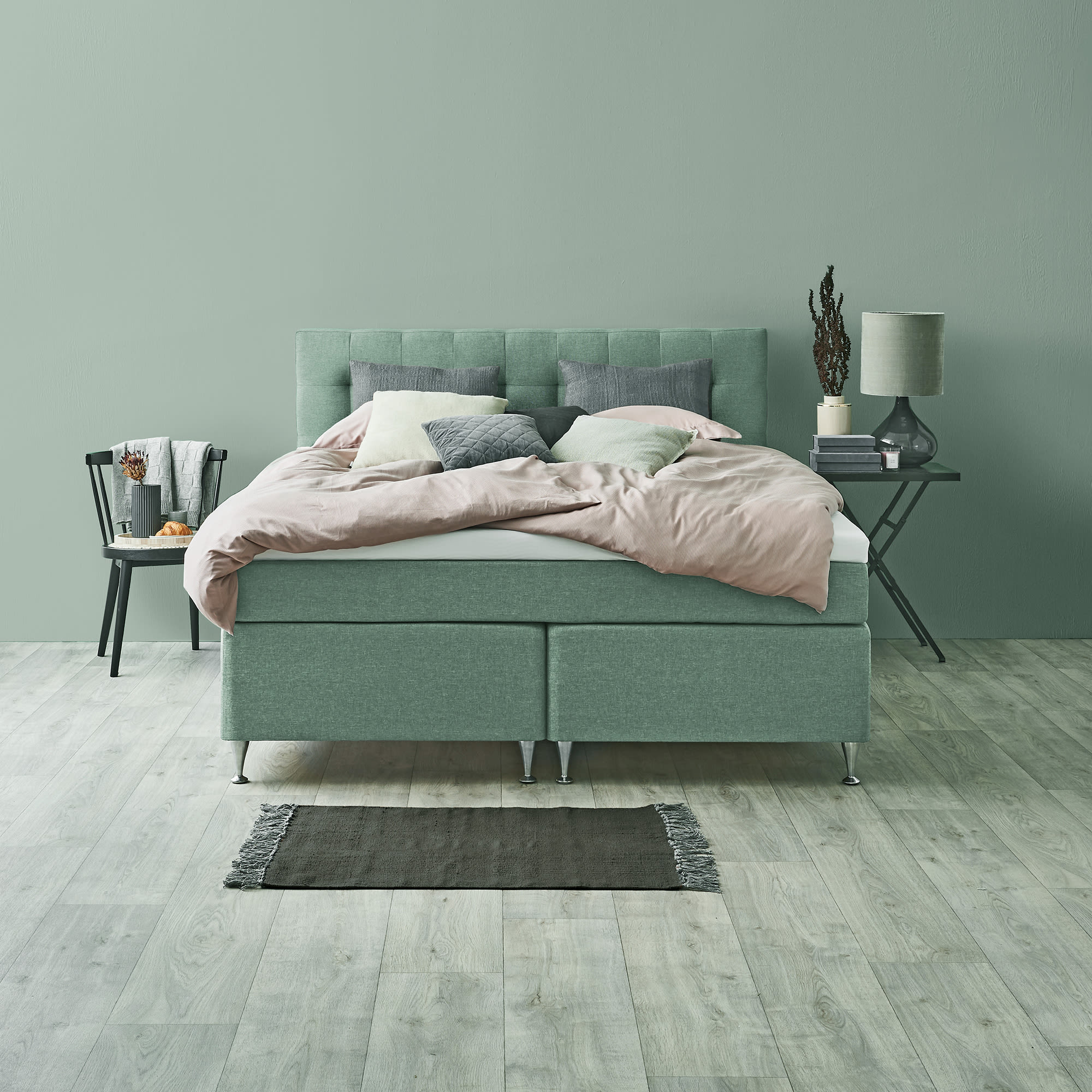 Grøn polstret seng med lyserødt sengetøj mod en lysegrøn væg i et soveværelse.