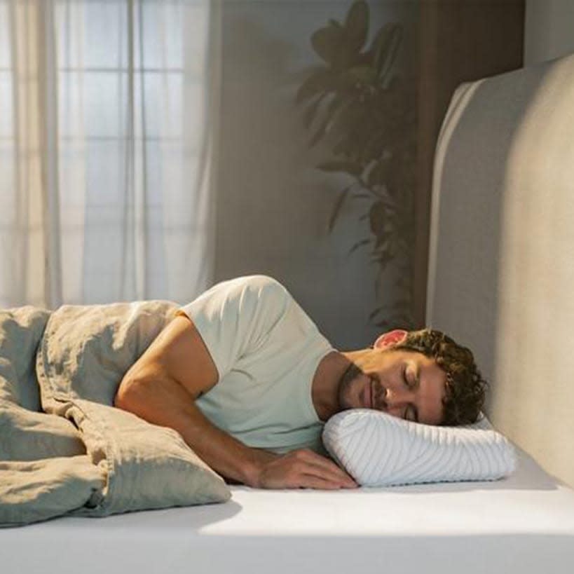 En mand sover fredfyldt på siden i sin seng med en ergonomisk hovedpude.