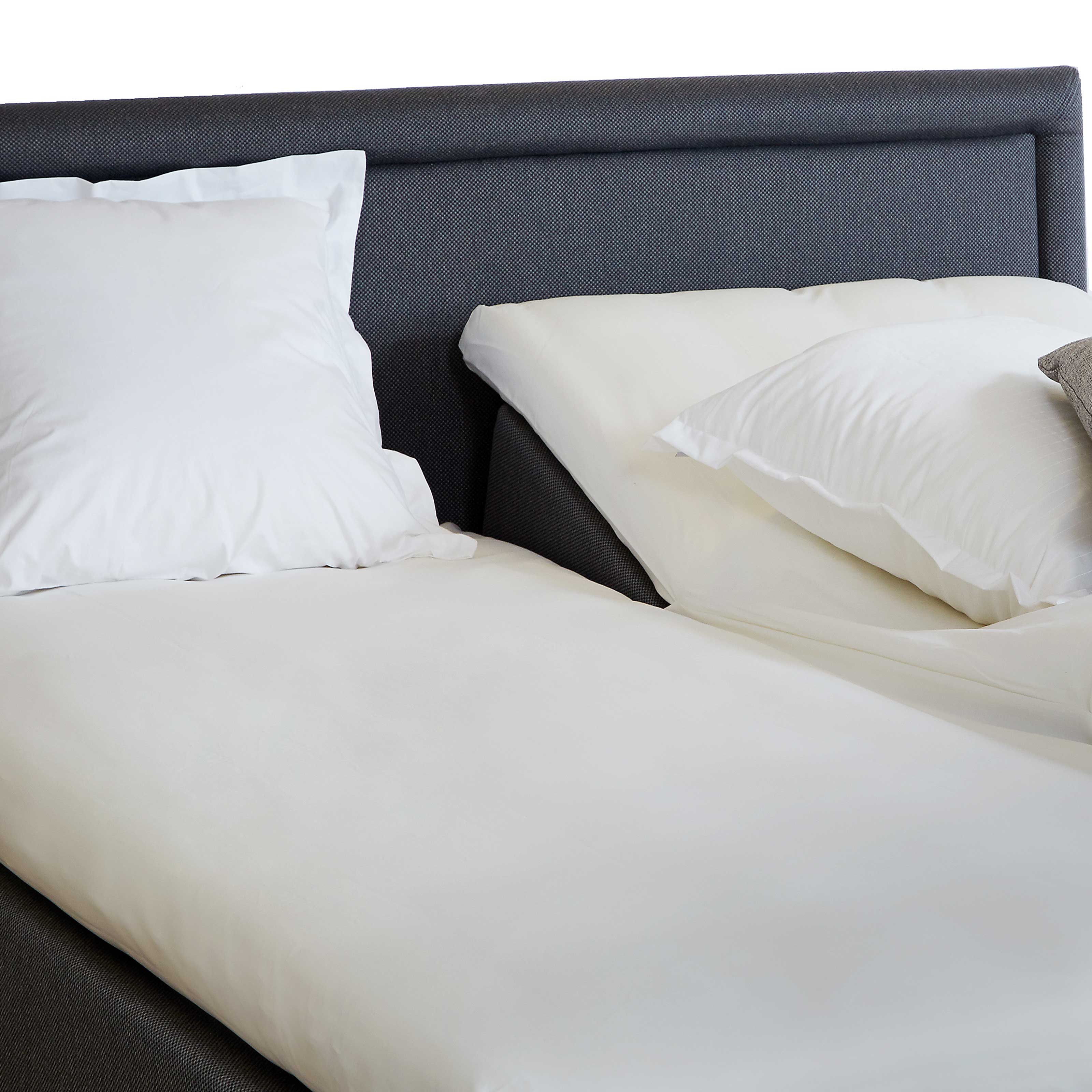 En seng med mørkegrå sengegavl og hvidt sengetøj, herunder puder og en dyne.