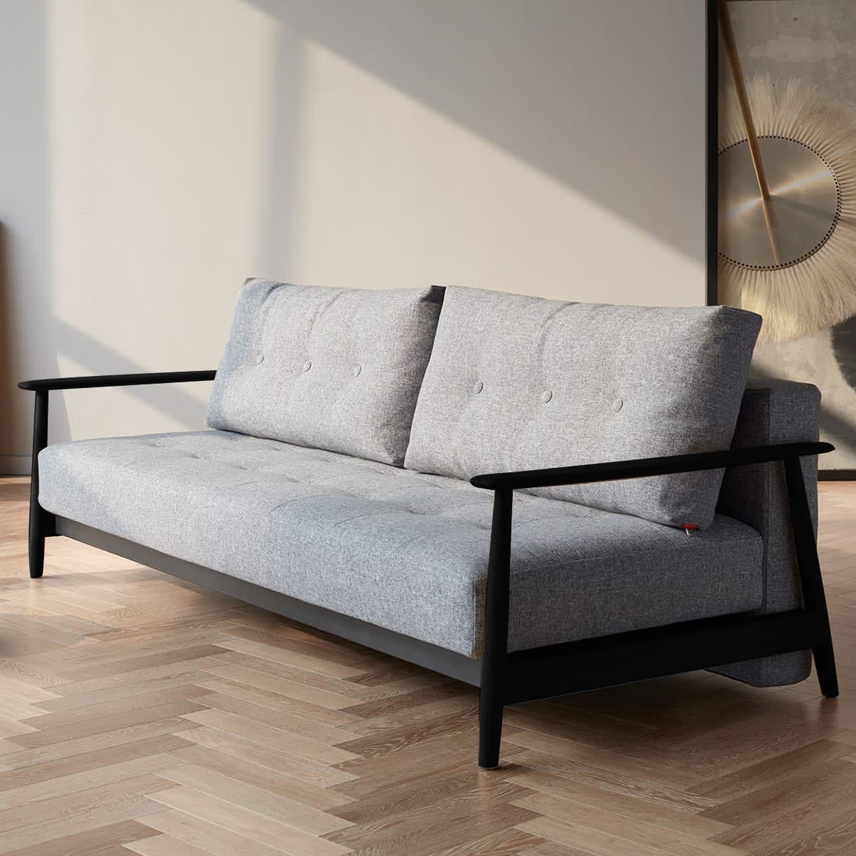 Moderne lysegrå sofa med sort træstel og knapper på et lyst parketgulv.