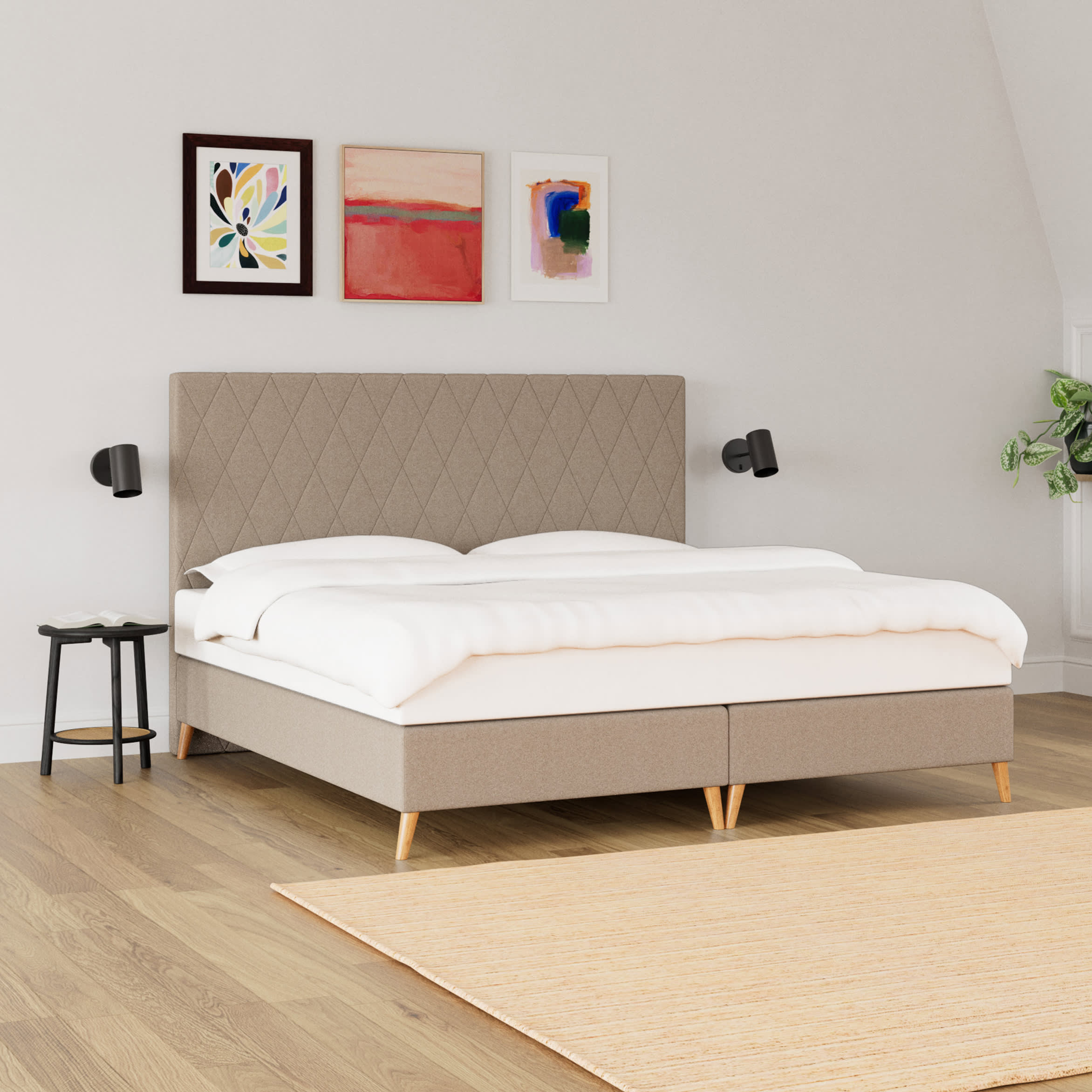 Et soveværelse med en seng med beige, quiltet sengegavl, hvidt sengetøj og tre farverige malerier på væggen.