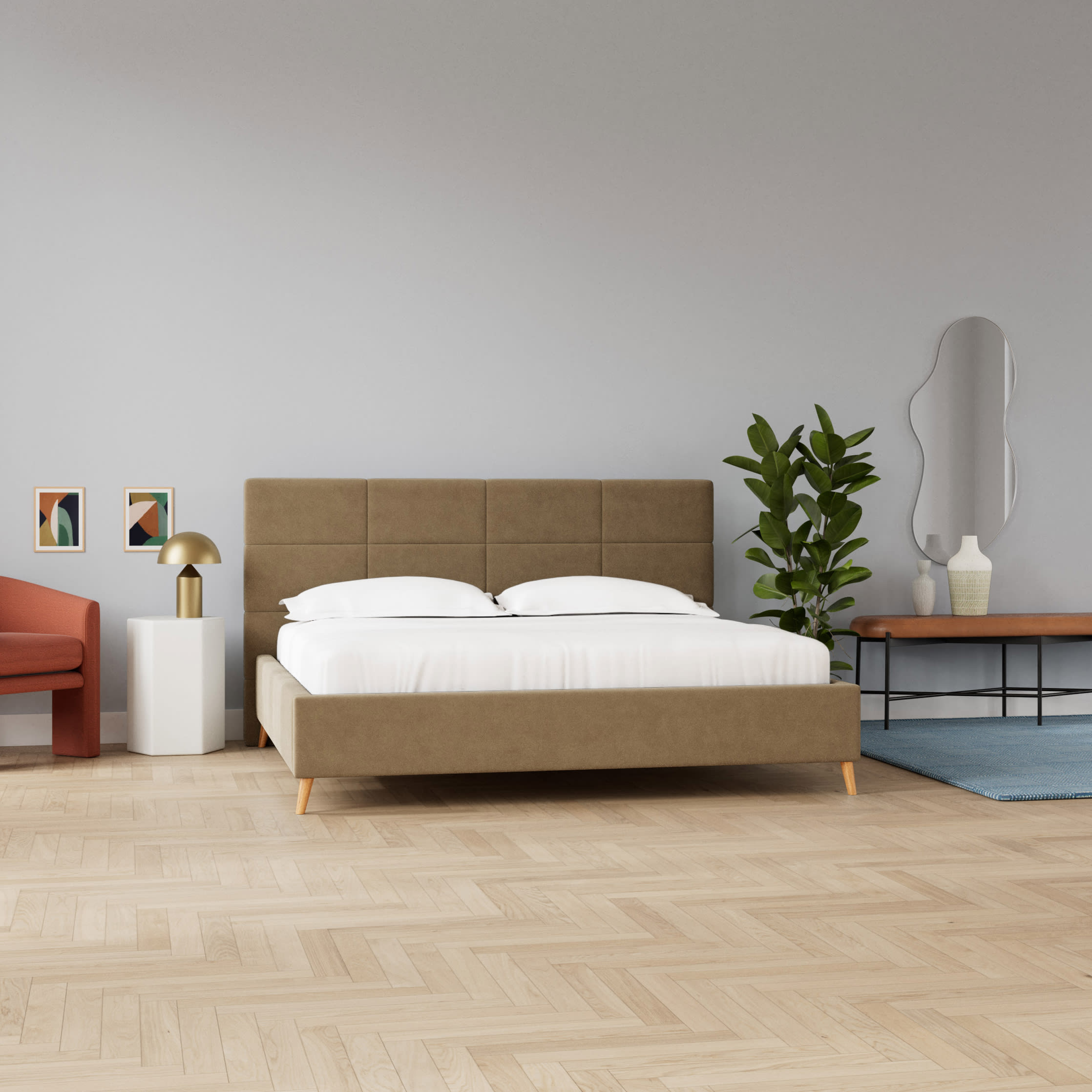 Moderne soveværelse med en brun polstret seng, hvidt sengetøj, en terracotta lænestol og en grøn plante på lyst trægulv.