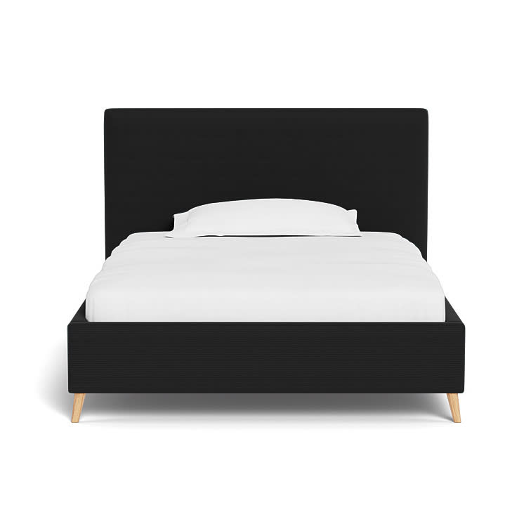 Sort enkeltseng med sengegavl, hvid madras og pude. Den har lyse træben.
