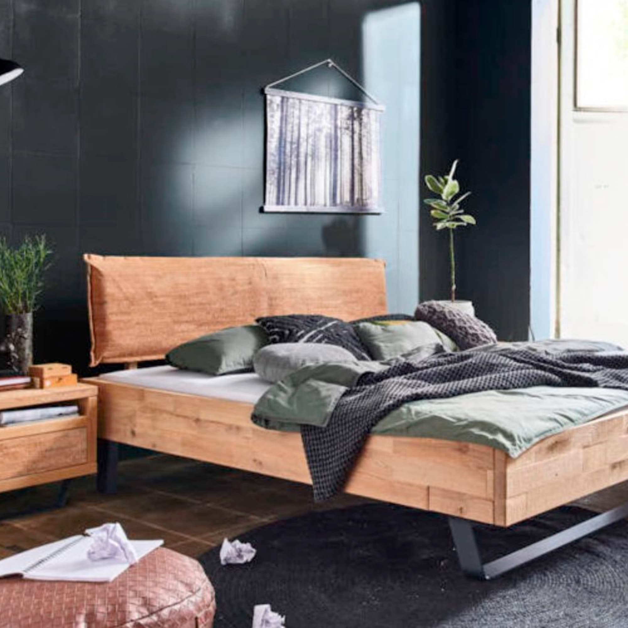 Et soveværelse med en træseng, grønt og gråt sengetøj, et sengebord og en skovplakat på væggen.