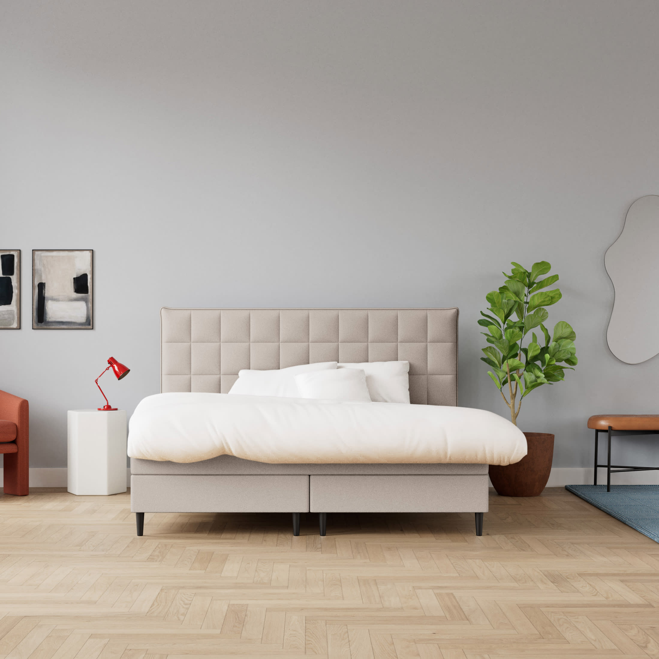 Et moderne soveværelse med en beige seng, hvidt sengetøj, en rød lampe, en stor grøn plante og abstrakt kunst på lysegrå vægge.