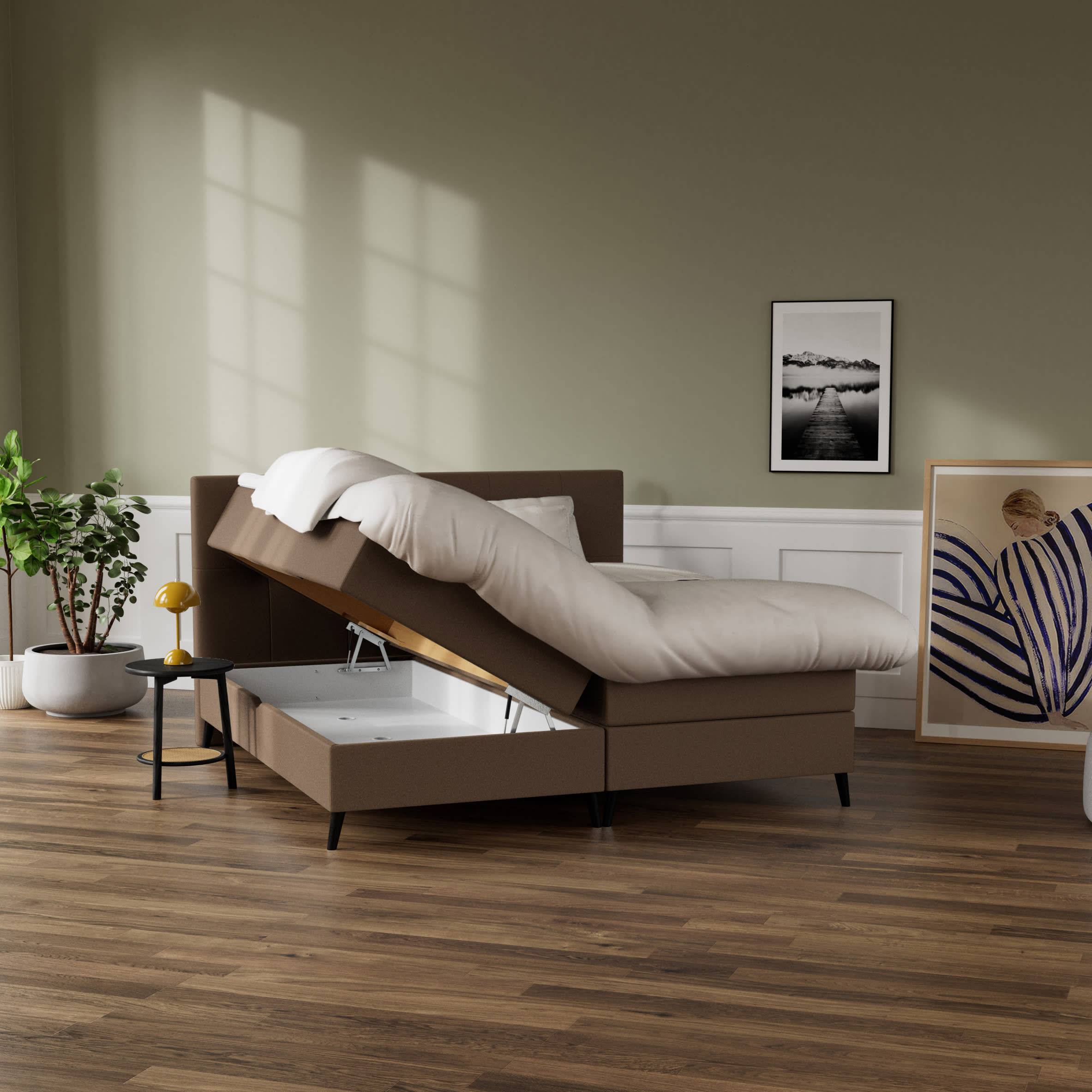 Brun opbevaringsseng med løftet madras, der viser hvidt opbevaringsrum. Et sengebord med lampe og plante står ved siden af.