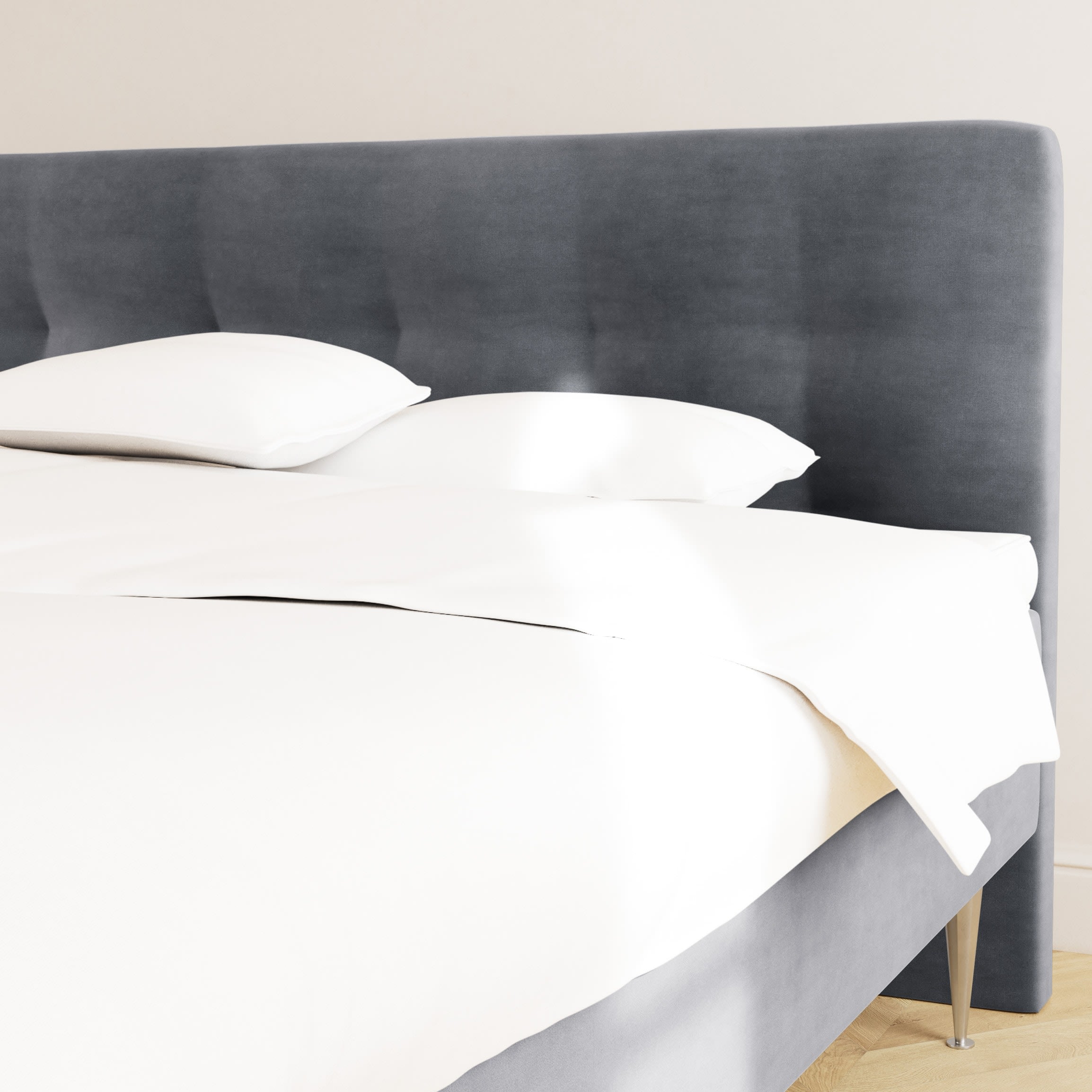 En seng med mørkegrå polstret sengegavl og hvidt sengetøj i et lyst værelse.