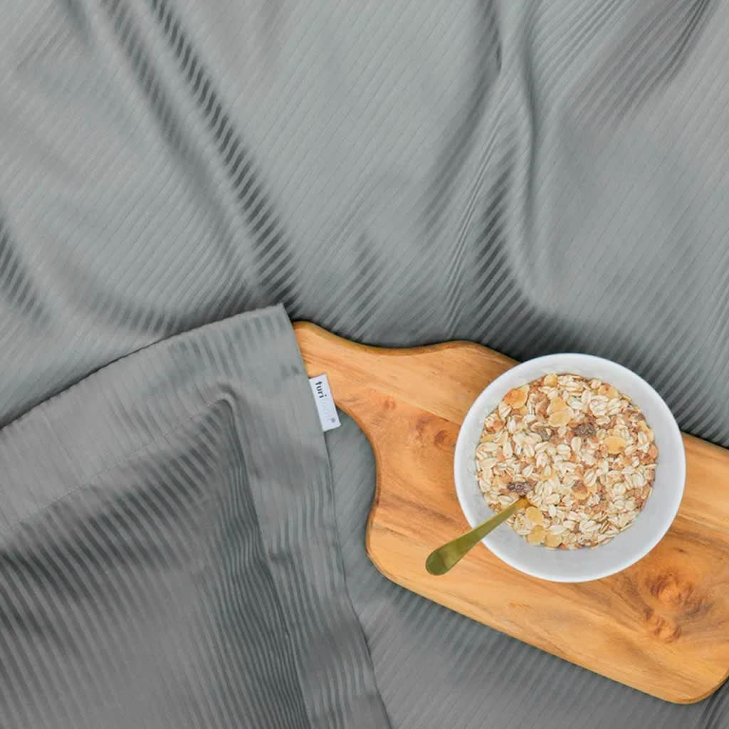 Gråt stribet sengetøj med et træserveringsbræt. På brættet står en skål müsli med en guld-ske.