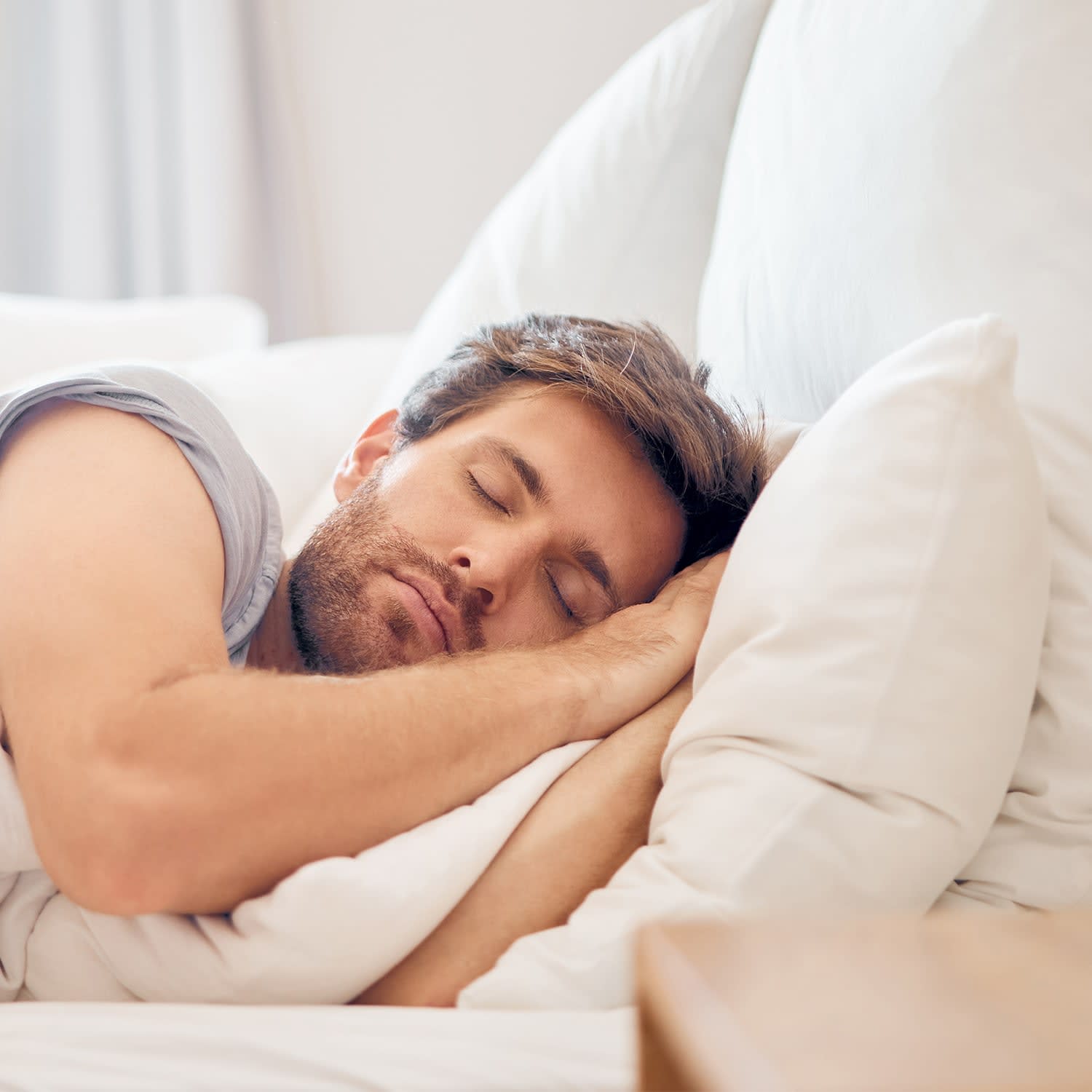En mand med skæg sover fredfyldt på siden i hvidt sengetøj.