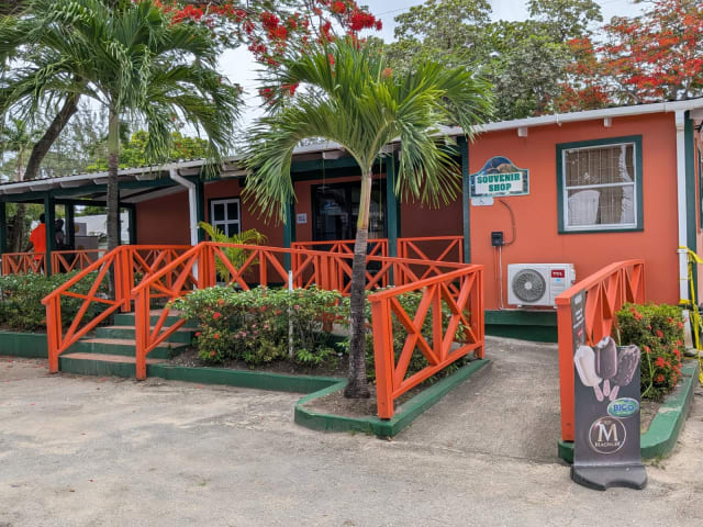 Orange-and-green souvenir shop with a visible shop sign and entrance ramp at Folkestone Beach in St. James, Barbados.