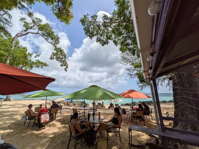 Shaded beachfront seating with tables and colourful umbrellas overlooking the sea at Sea and Sand Bar, Folkestone Beach, Barbados.