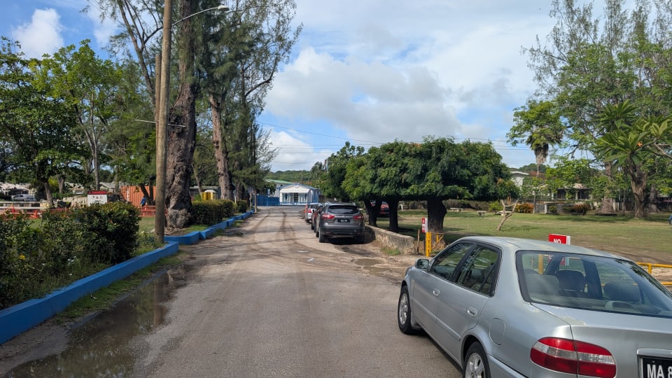 Street entrance leading into Folkestone Beach, with parked cars and blue-painted curbs in St. James, Barbados.