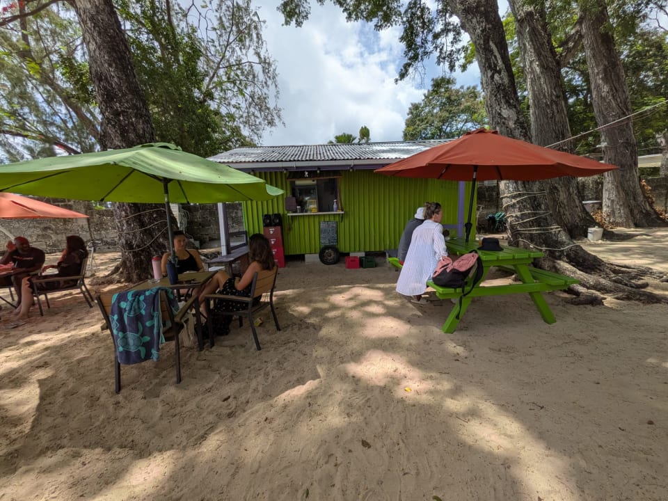 Lime-green Sea and Sand Bar with shaded tables, colourful umbrellas and customers seated on the sand at Folkestone Beach, Barbados.