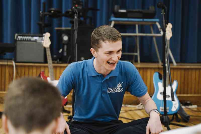 band coach in blue shirt sitting cross legged and smiling