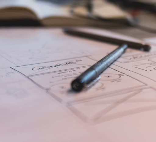 A pen laid over a piece of paper. On the paper are several concept drawings