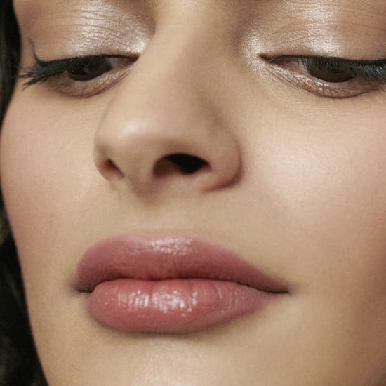Close-up of a woman's face with glossy nude-pink lips and shimmering eye makeup.