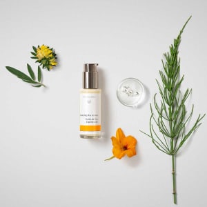 Balancing Day Lotion bottle with flowers, herbs and a glass dish on a white background.