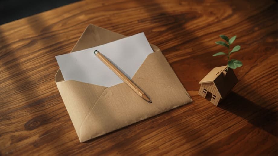 Sobre con documentos y lápiz junto a una casita con un brote naciendo