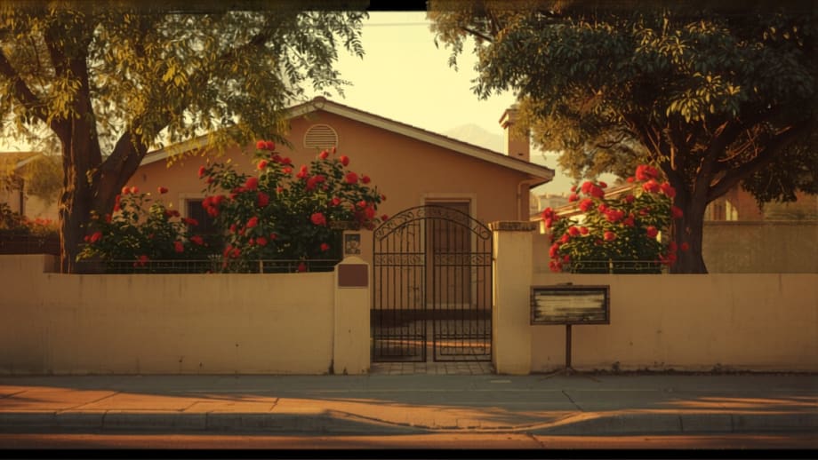 Casa de estuco con reja de fierro, rosales y cartel de madera en blanco