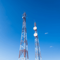 Deux tours de télécommunication rouges et blanches équipées d'antennes paraboliques, se dressent sous un ciel bleu dégagé avec quelques nuages.