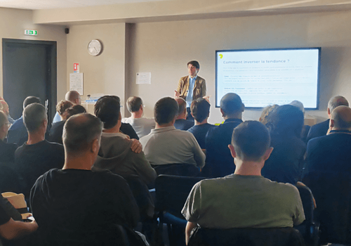 Une présentation en salle de conférence chez France Travail. Un homme présente devant un écran à un public assis, vu de dos.