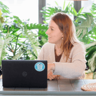 Femme présentant le bilan carbone dans les bureaux Extia, assise à une table devant son ordinateur, entourée de plantes vertes et lumière naturelle.
