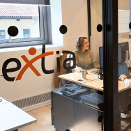 Vue sur les bureaux Extia Milano à travers une vitre logotée. Deux collaboratrices échangent en open space.