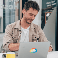 Homme concentré devant son ordinateur orné d’un sticker Google Cloud, dans une salle vitrée avec une tasse jaune posée devant lui.