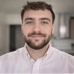 Portrait de Maxime Chauvet. Il porte une chemise rose et blanche. Il est souriant.