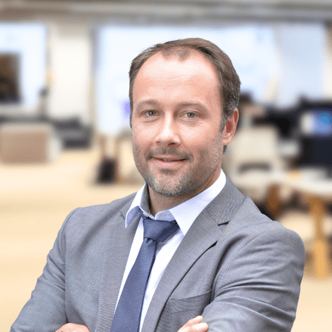 Portrait de Guillaume Carmen, Directeur de l'offre apiniX & KAM Orange groupe. Il est souriant et porte un costume gros, une cravate bleue et une chemise blanche.