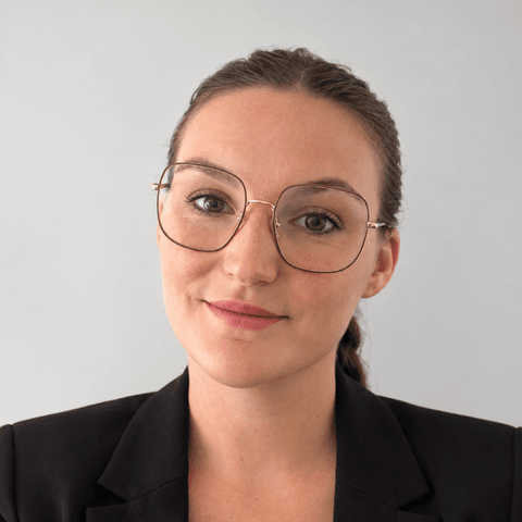 Portrait de Gabrielle VERNEUIL, Lead développpement. Elle est souriante et porte une veste de costume noire ainsi que de grandes lunettes arrondies.