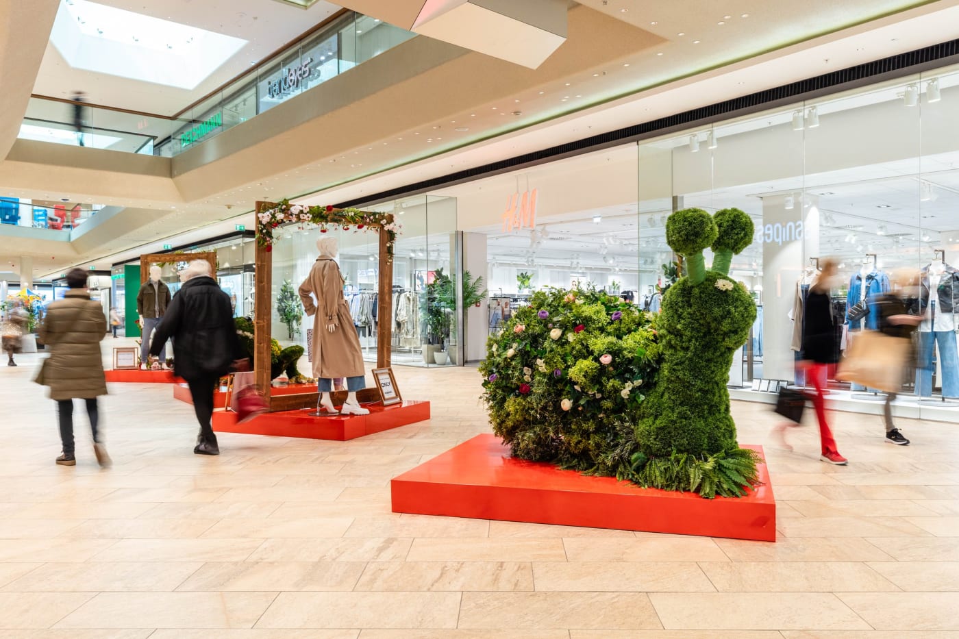 FRAMES mit botanischer Schnecken-Figur in einer Mall, Besucher gehen vorbei