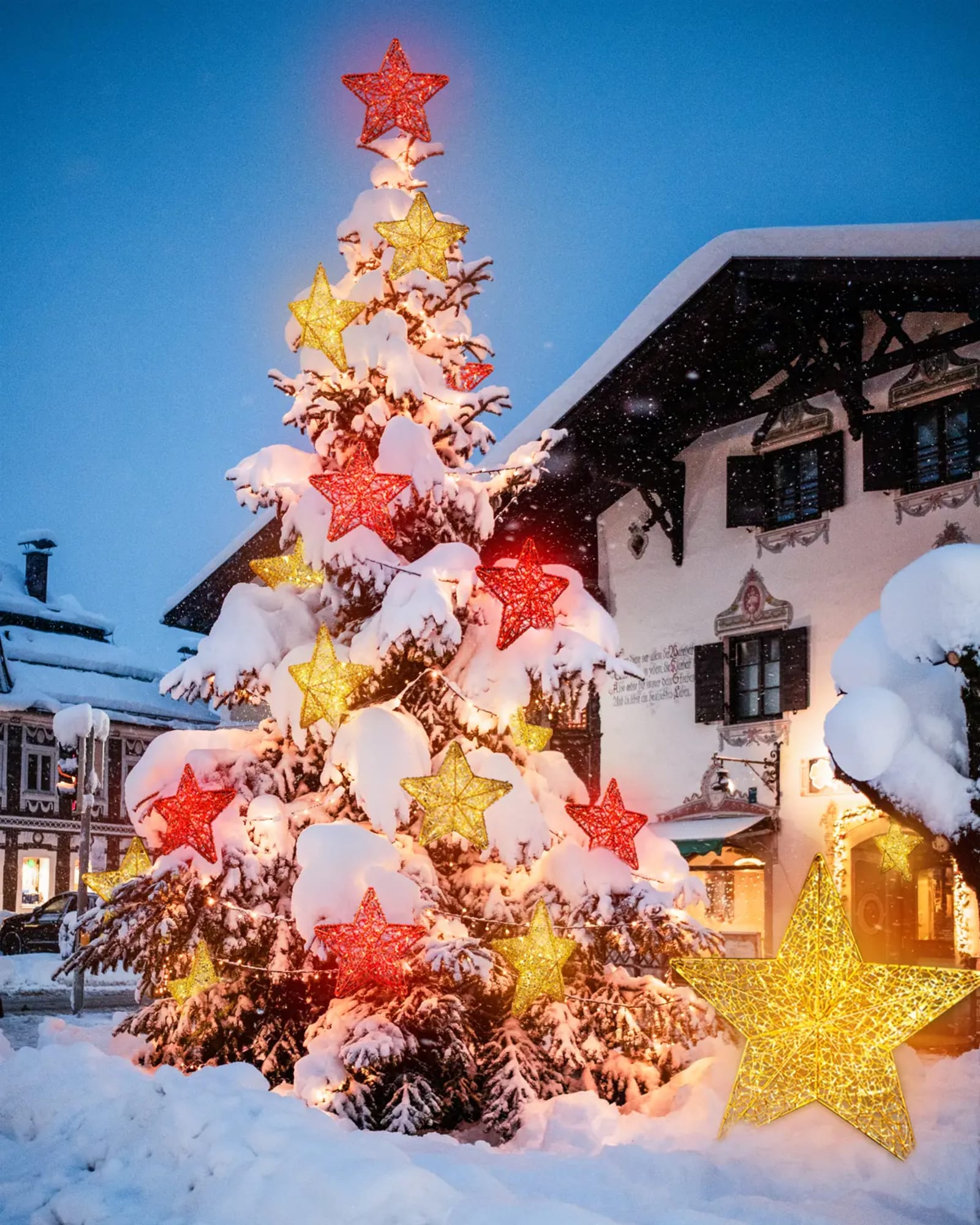 Beleuchteter Tannenbaum vor einer Alpenfassade am Winterabend