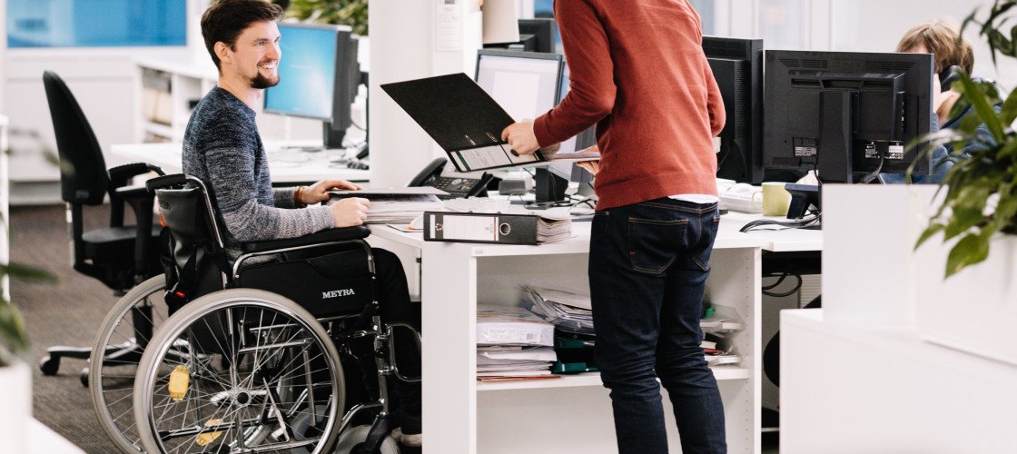 A man is sitting in a wheelchair working in an office. A man is sitting in a wheelchair working in an office.