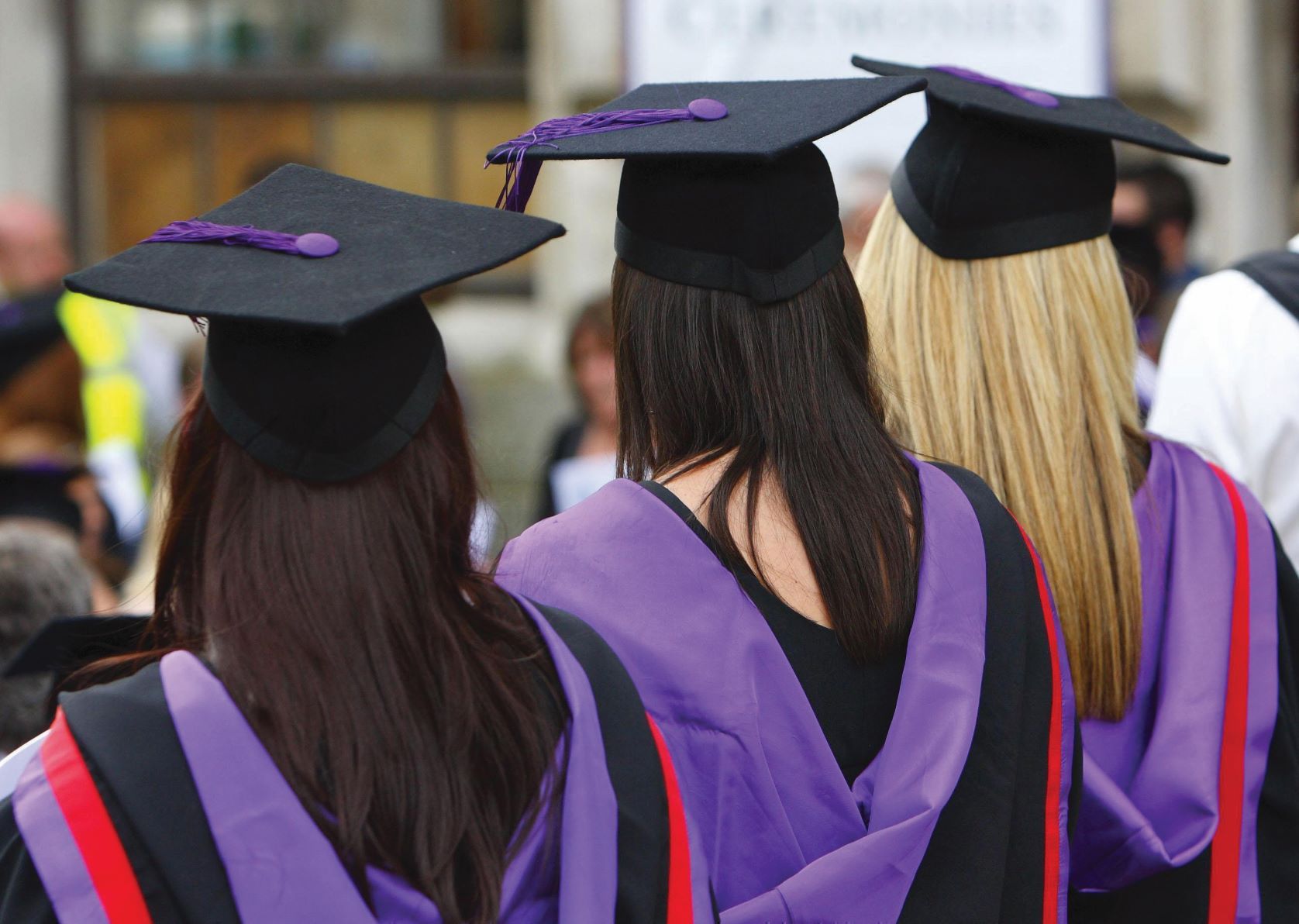 University graduation Three female students stand with their backs facing the camera in full graduation gowns and caps