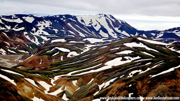 A dramatic waterfall cascades over rugged cliffs into a misty, moss-covered Icelandic canyon
