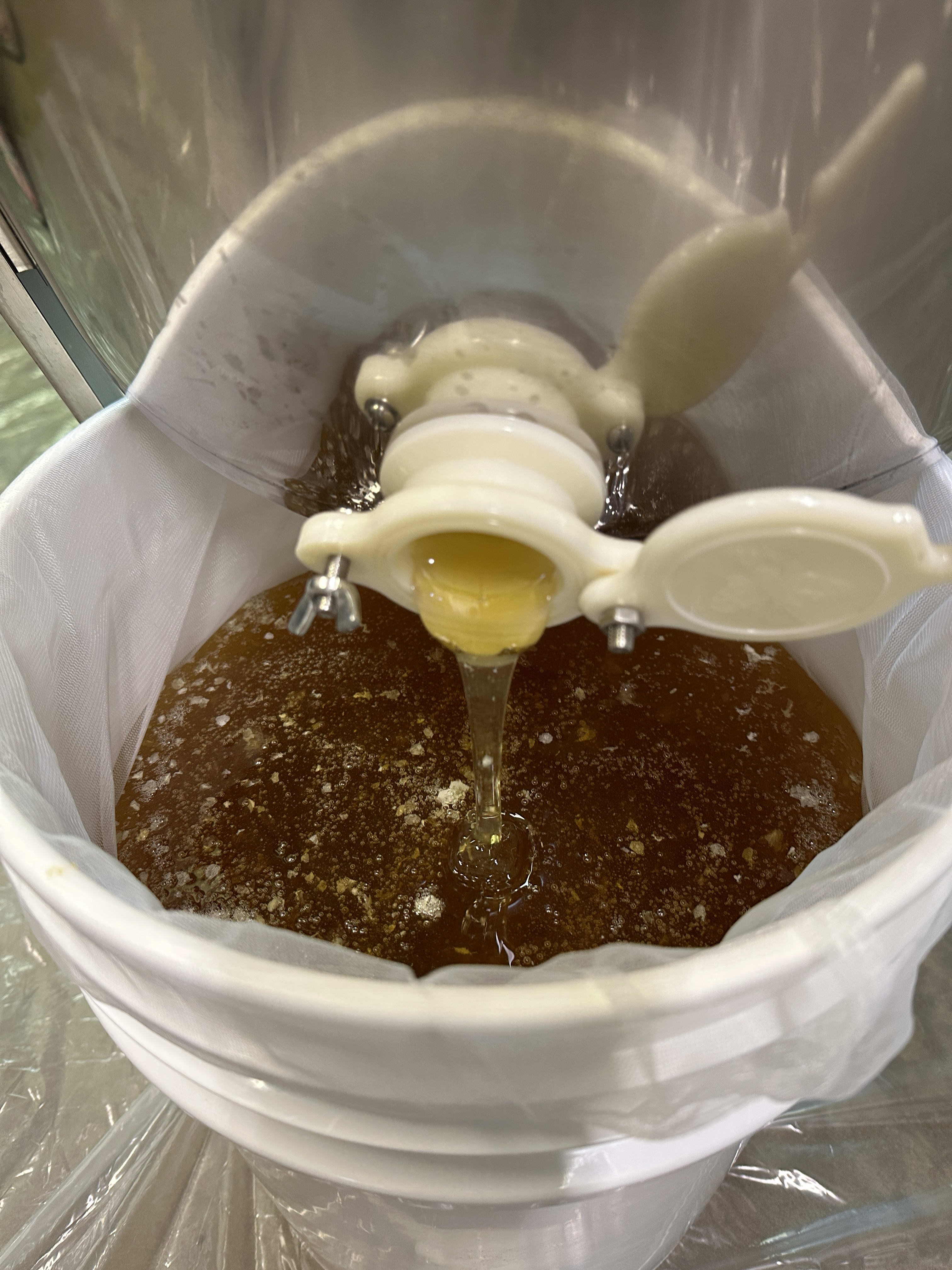Honey extractor in operation, with honey flowing through a spigot into a filtering sieve held by a bucket.
