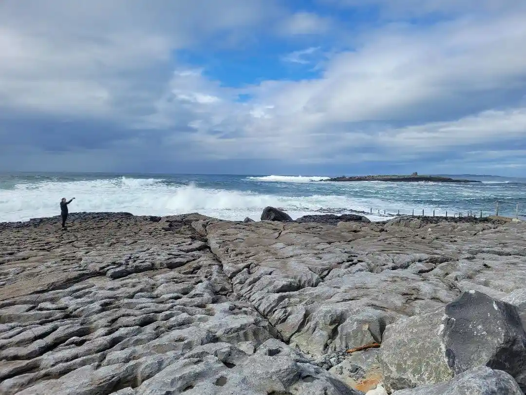 Doolin pier - Person stood on rocks next to the blue ocean with crashing waves.