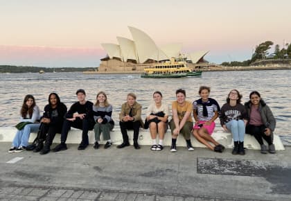 Students from the Anzac tour are sitting on a ledge in front of the Sydney Opera House