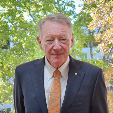 Dr Ian Watt AC wearing a suit and positioned in front of trees.