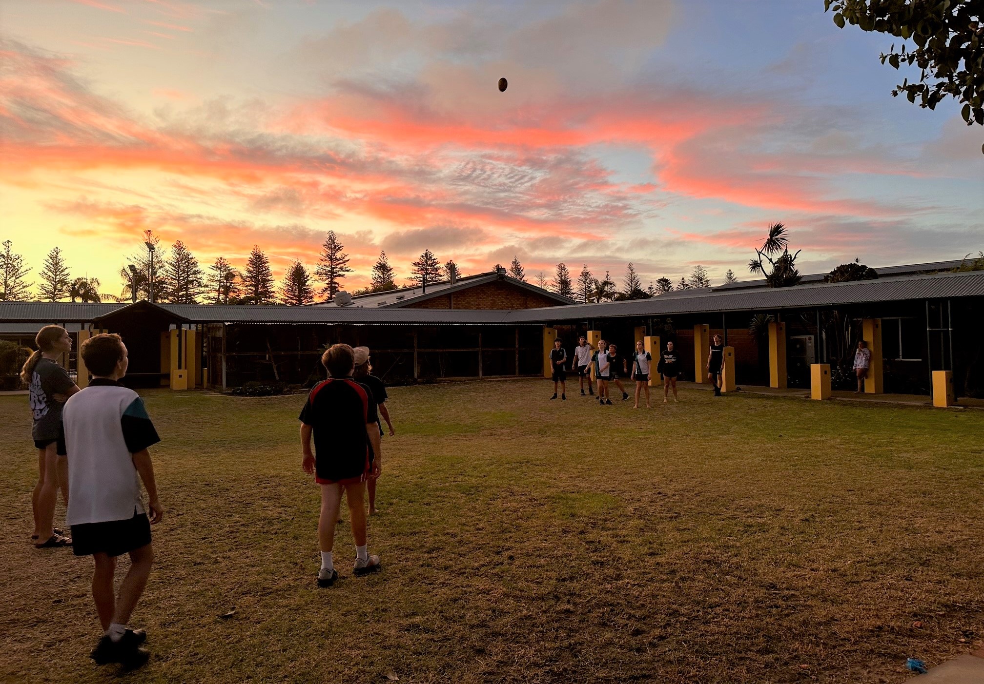 Students playing footy on the college grassy area in the sunset