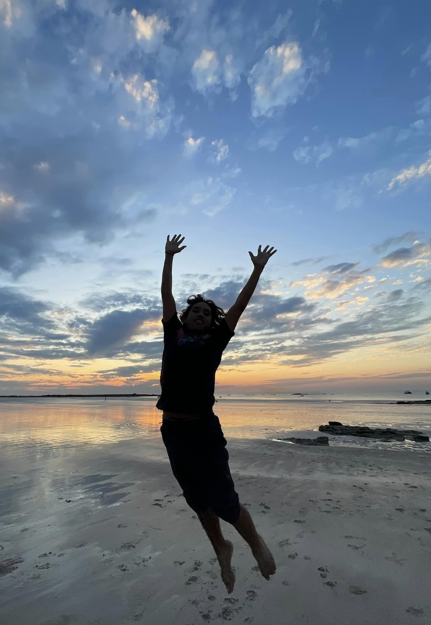 Happy student jumping for joy in front of a beautiful Broome sunset