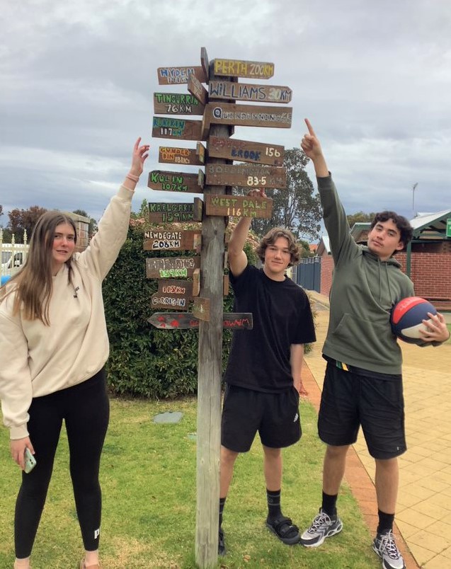 Narrogin Residential College boarders standing beside a signpost indicating distances to nearest towns