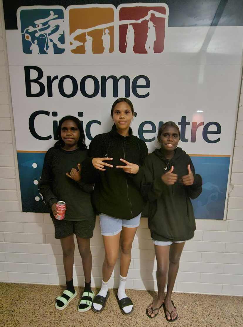 3 happy Broome Residential College boarders standing in front of the Broome Civic Centre sign 