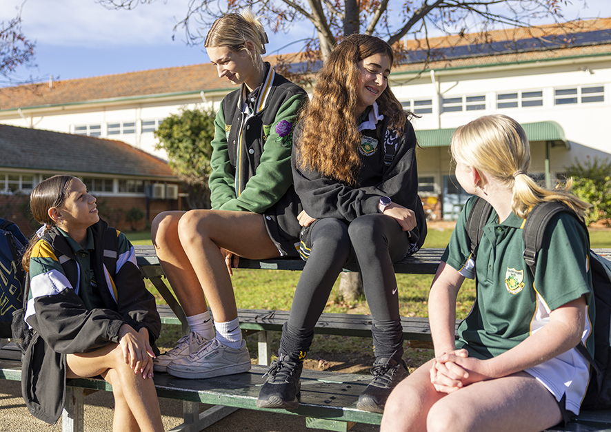 Group of smiling Narrogin Residential College boarders sitting on a school bench.