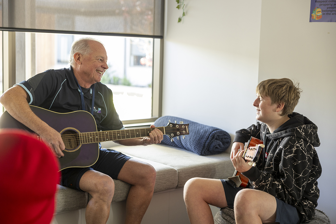 Boarding supervisor at Moora Residential College playing guitar alongside a student. 
