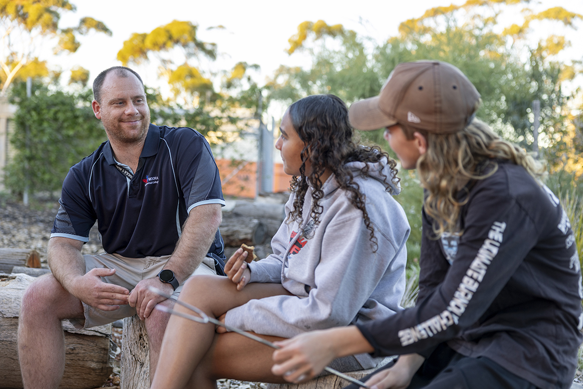 Boarding supervisor sitting with students toasting marshmallws at Moora Residential College.