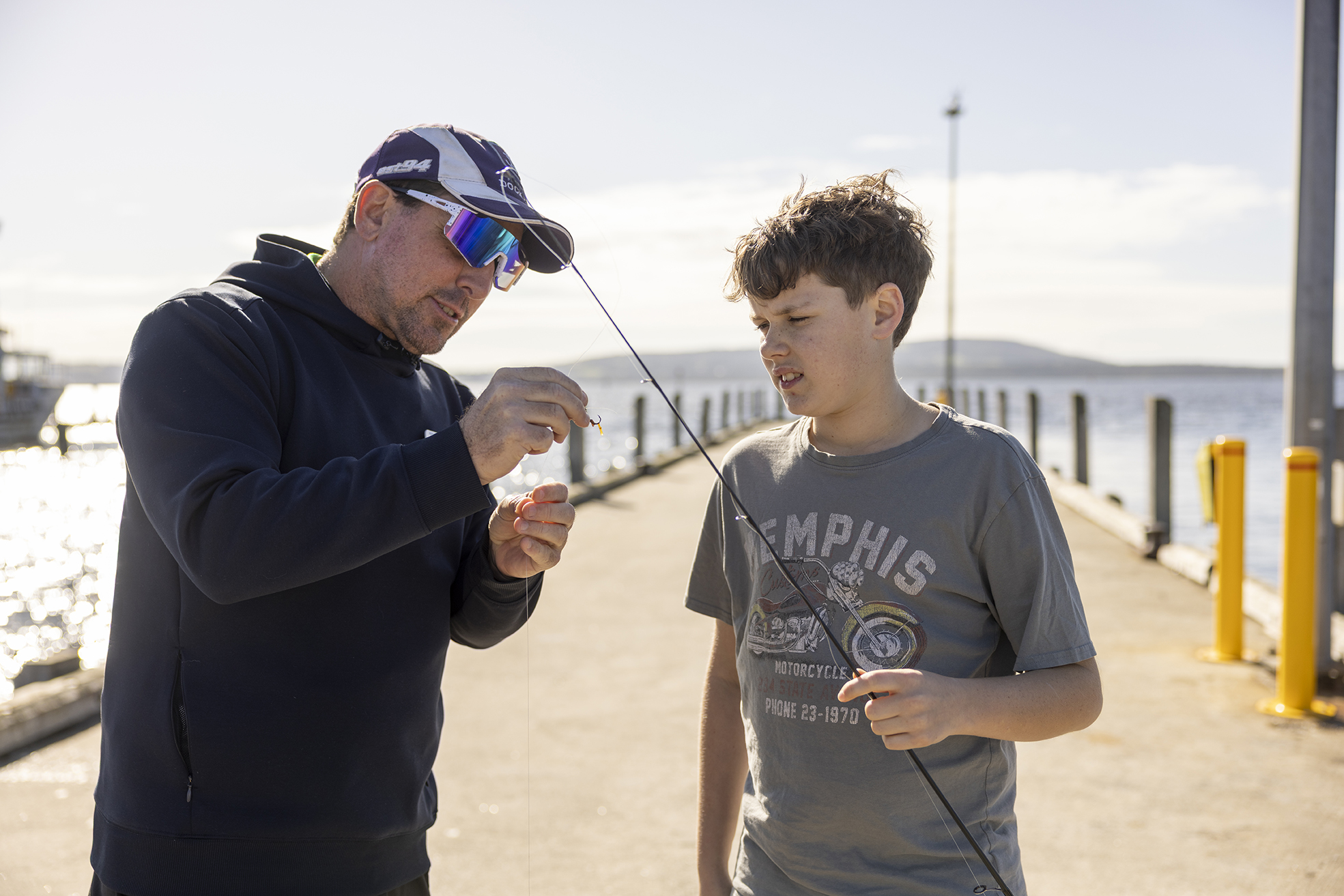 A boarding supervisor from Albany Residential College helping a boarder tie a fish hook onto a fishing rod.