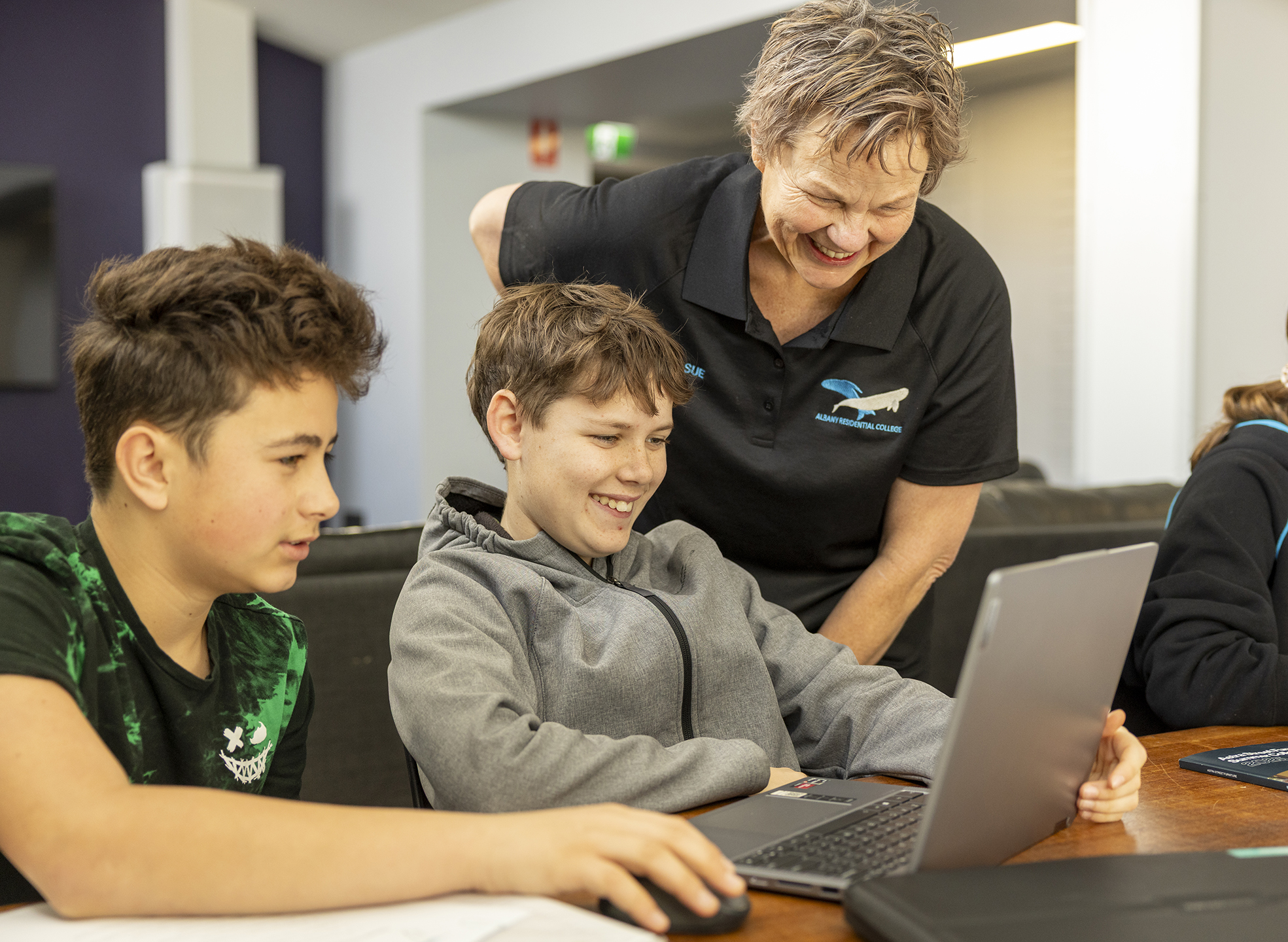 A boarding supervisor from Albany Residential College looking at a computer with students.