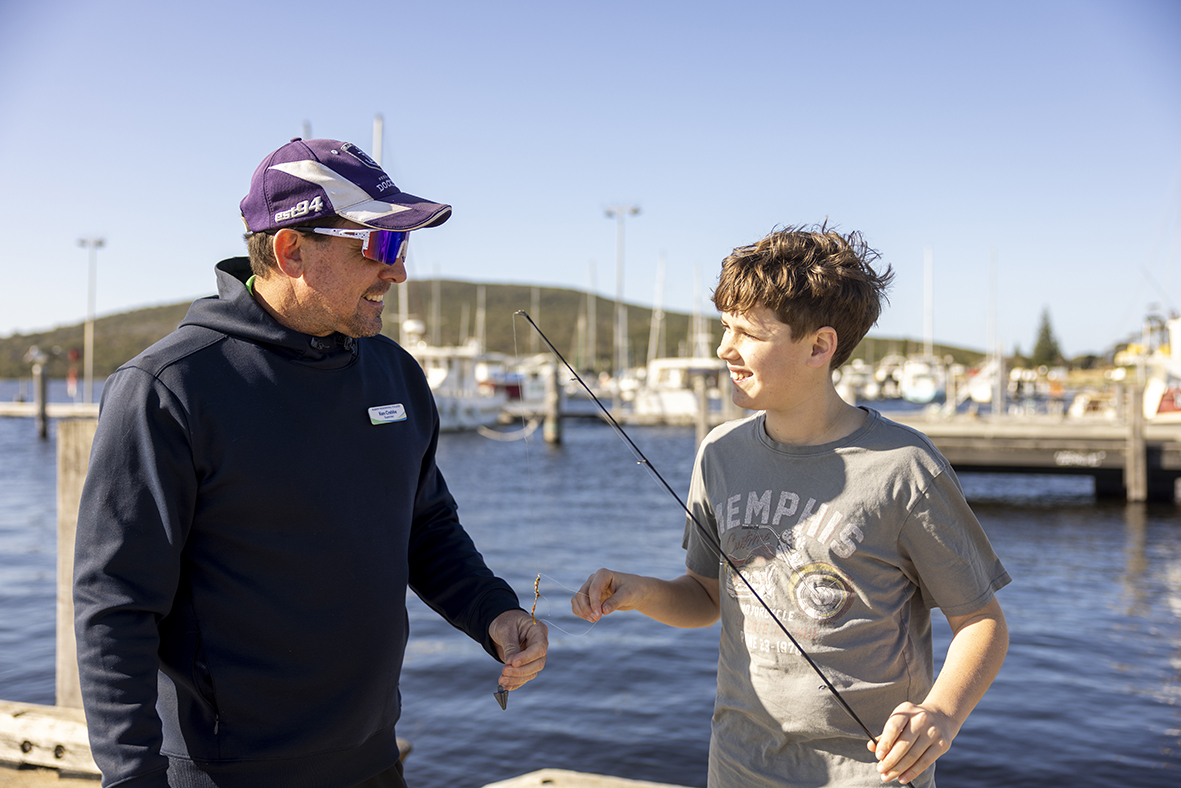 A smiling boarding supervisor from Albany Residential College helping bait a fishing line for a boarder.